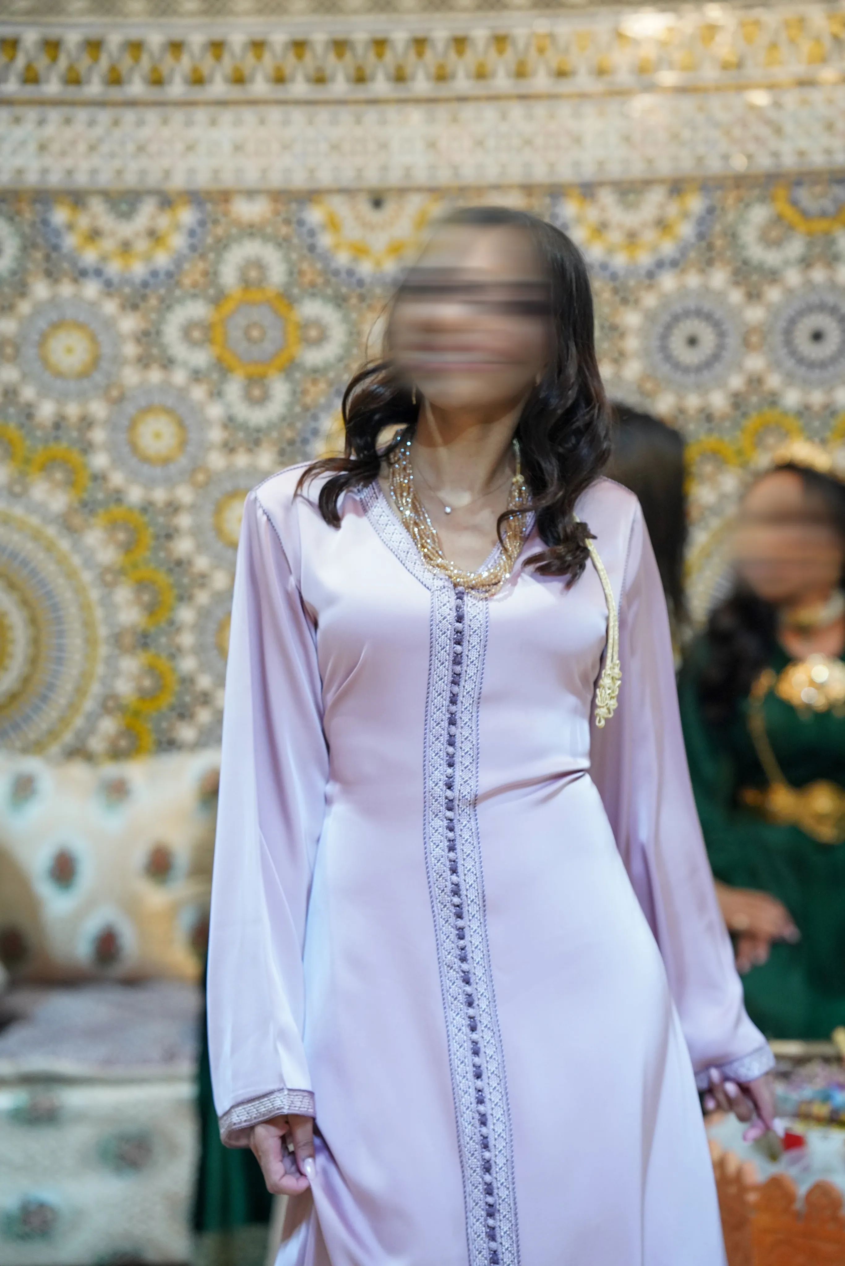 Caftan rose poudré porté devant un mur de zellige marocain